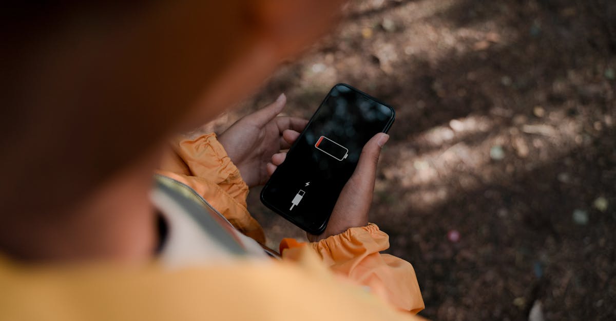 Teenage boy holds a smartphone displaying low battery outdoors in a forest.