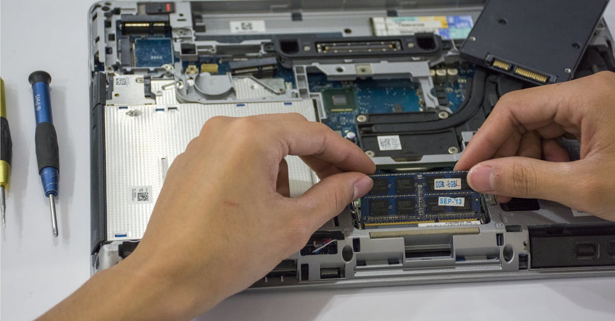 Close-up of a technician assembling a laptop's internal components using tools.
