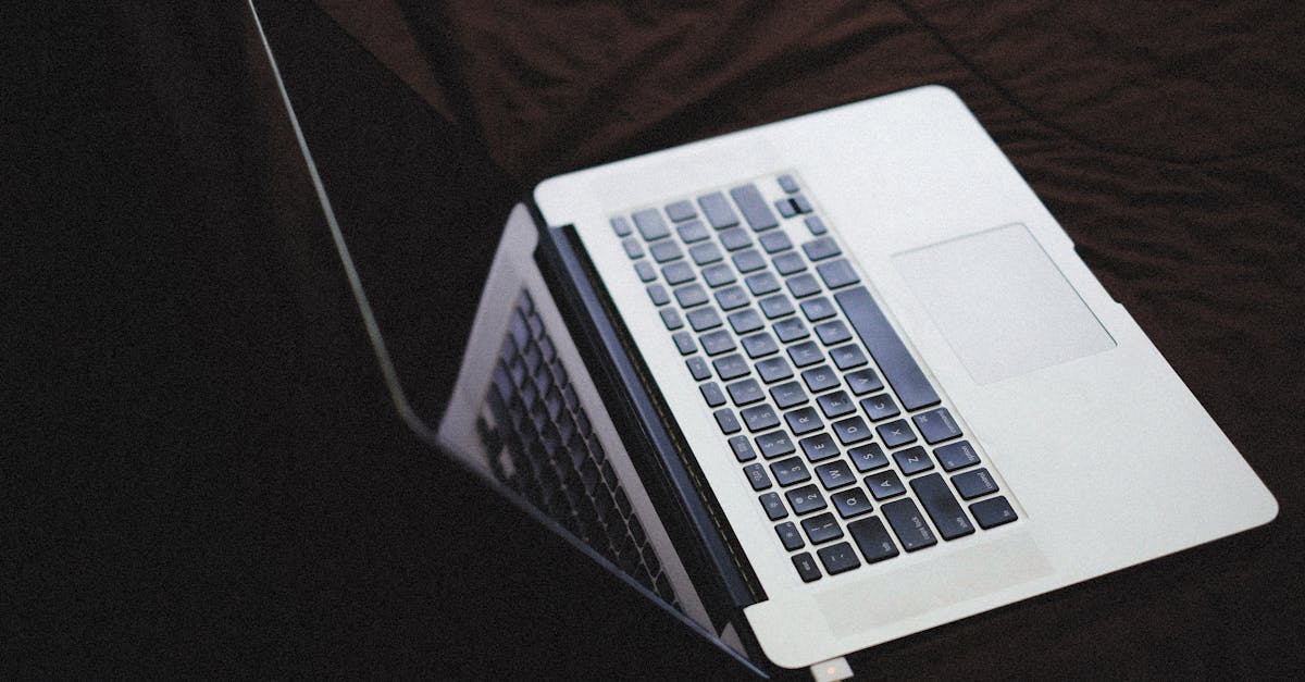 Modern laptop with backlit keyboard on a dark fabric surface, connected to a charger.