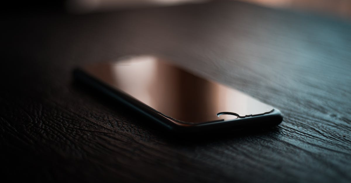 A smartphone lies on a dimly lit wooden table showcasing reflection and shadows.