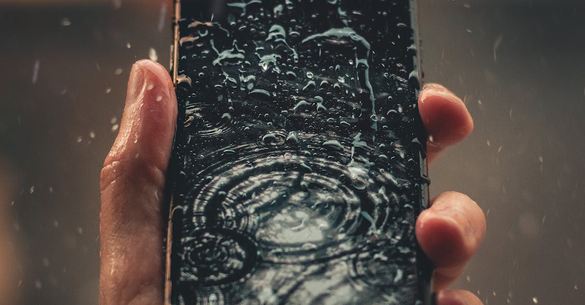 A person holds a smartphone with raindrops on screen, emphasizing water resistance.