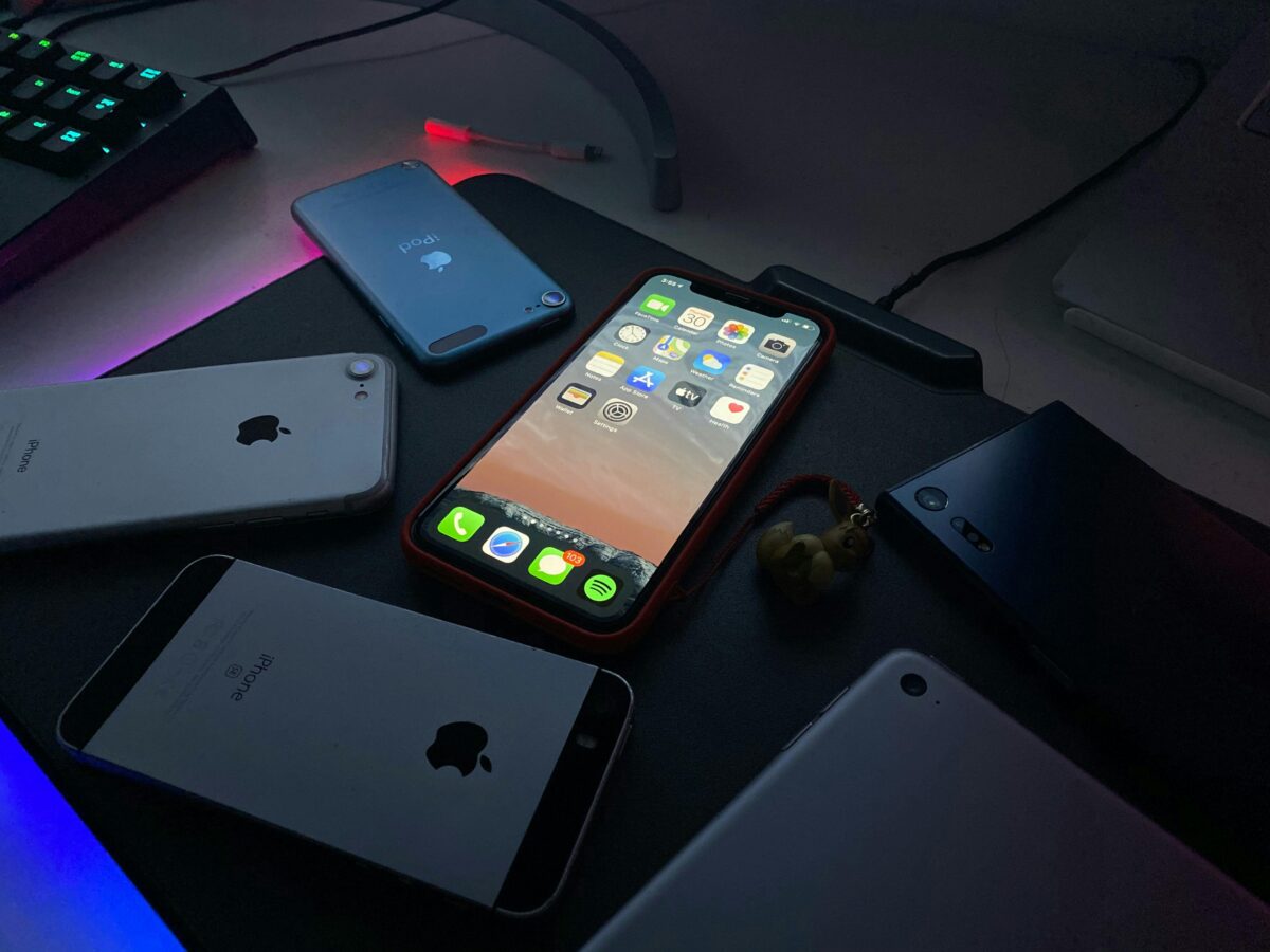 Close-up of various Apple devices on a desk illuminated by dim light.
