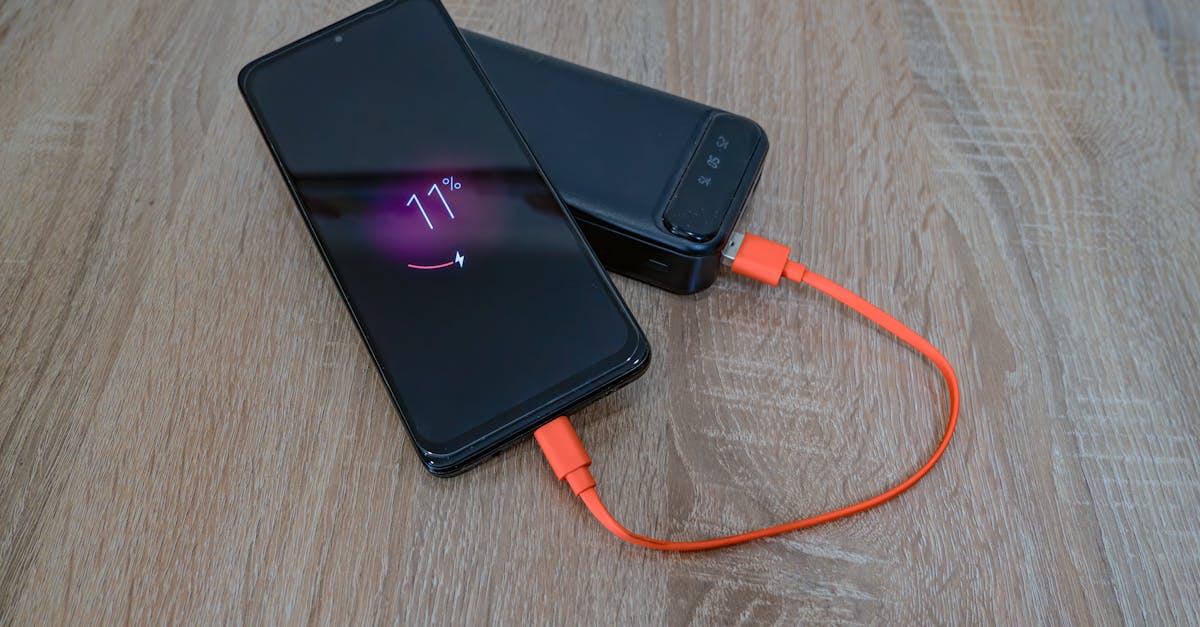 A smartphone charging from a power bank with an orange cable on a wooden table.