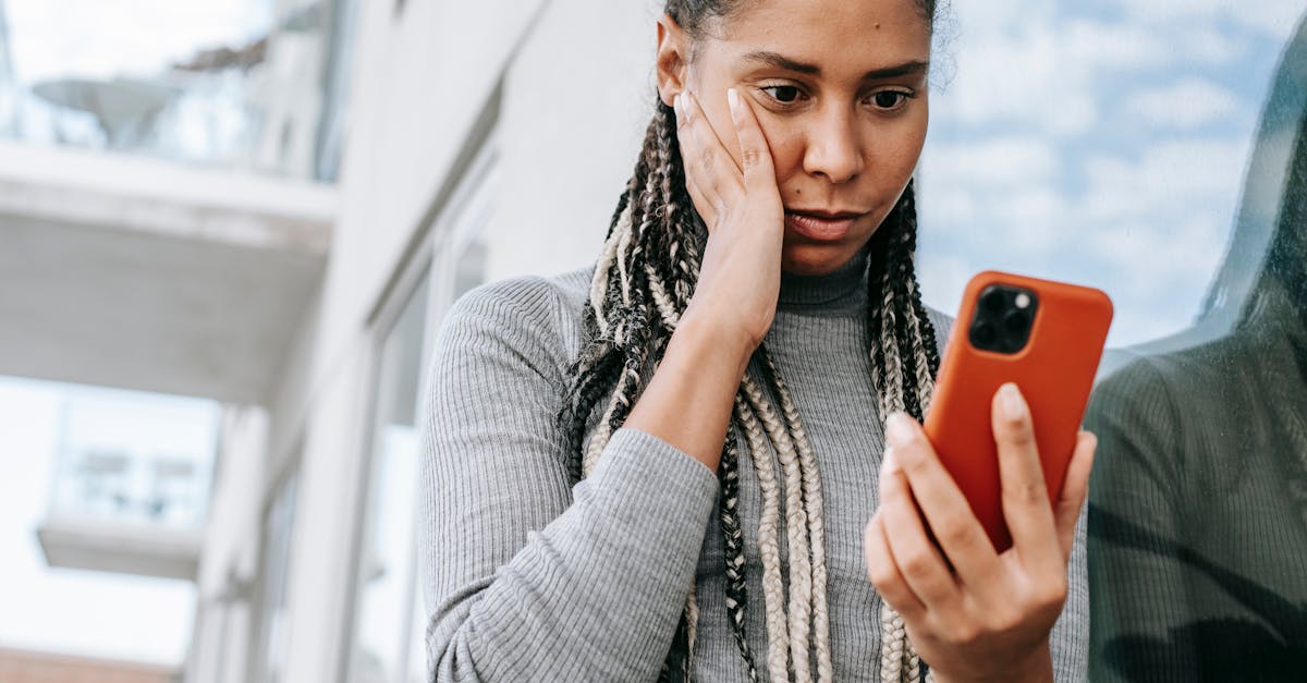 Crop serious African American female with dreadlocks touching cheek in contemplation and browsing mobile phone on street
