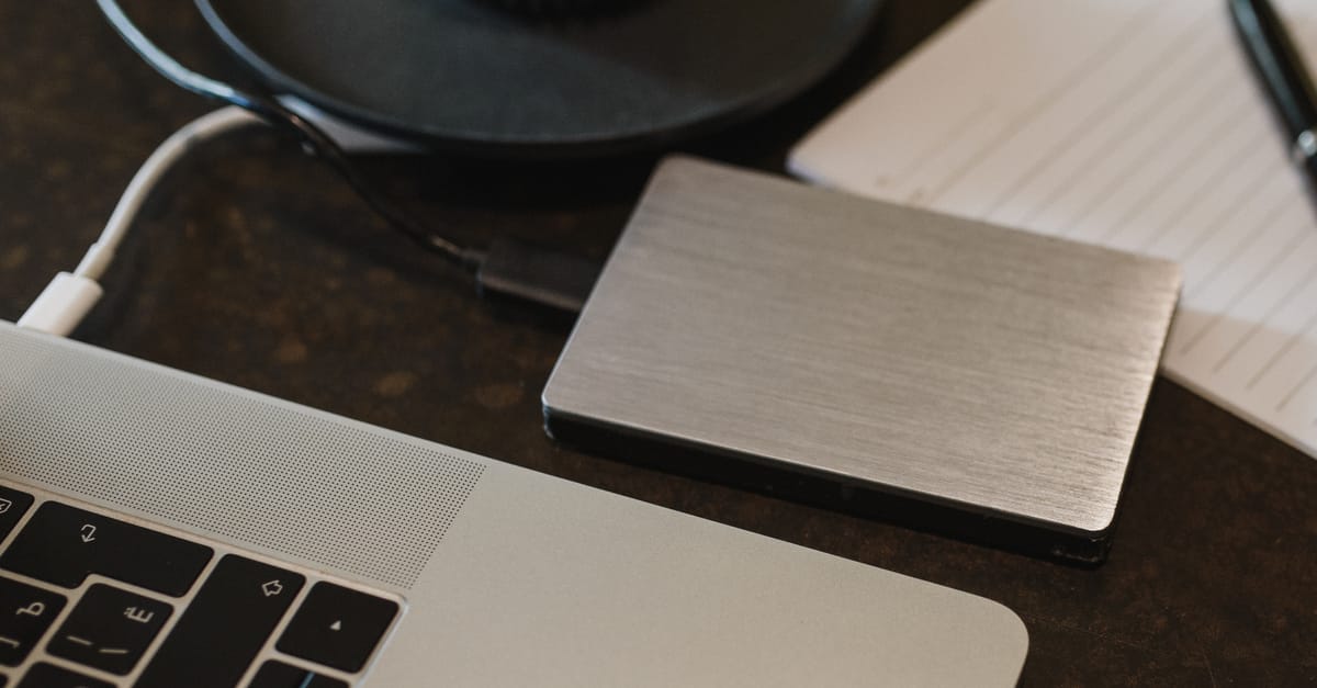 Closeup of an external hard drive connected to a laptop with a USB cable on a desk.