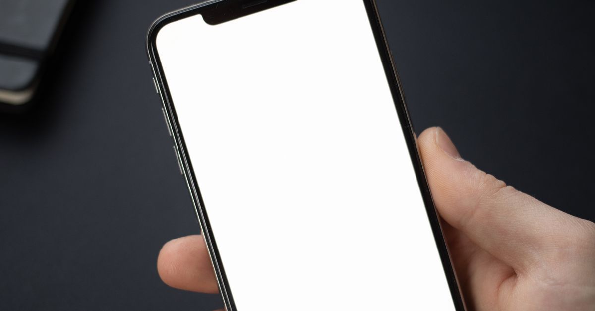 Close-up of a hand holding a smartphone with a white blank screen, ideal for mockup.