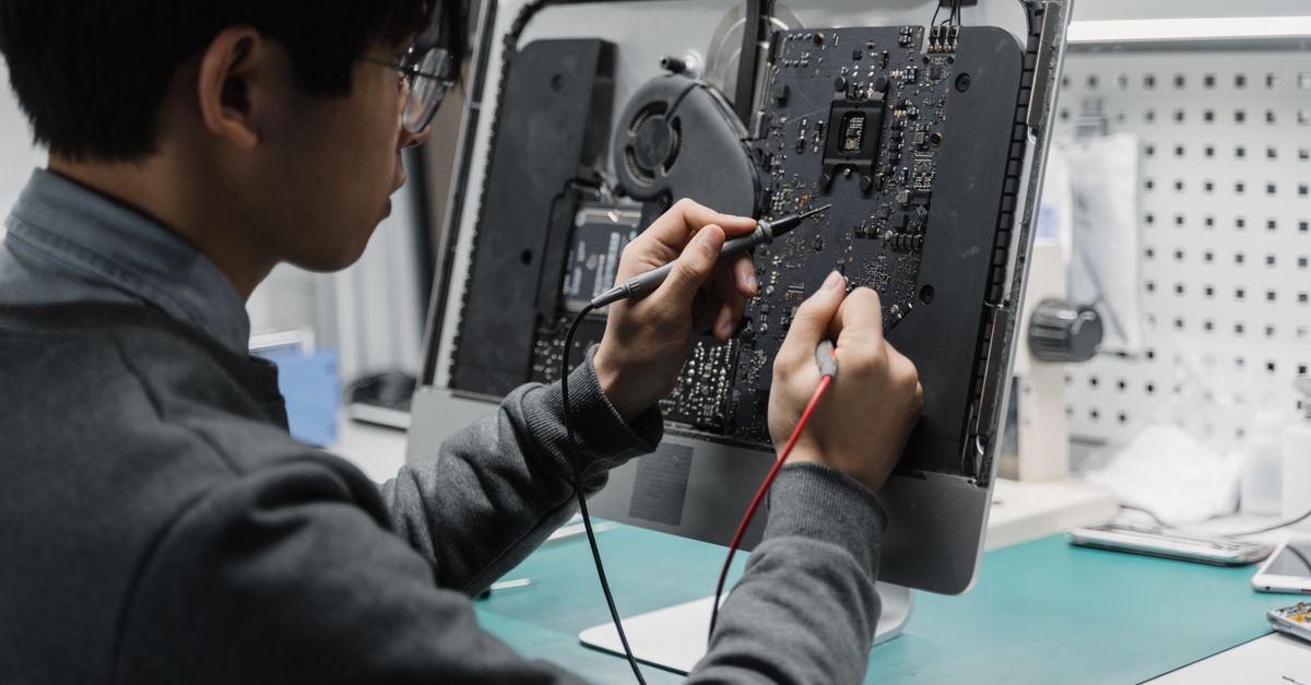 A technician works on a computer motherboard using tools at a workspace, focusing on electronics repair.