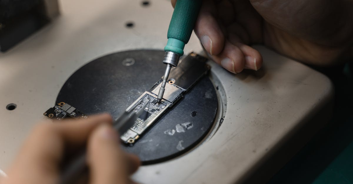 Hands using a soldering iron on circuit board, showcasing precise electronic repair indoors.