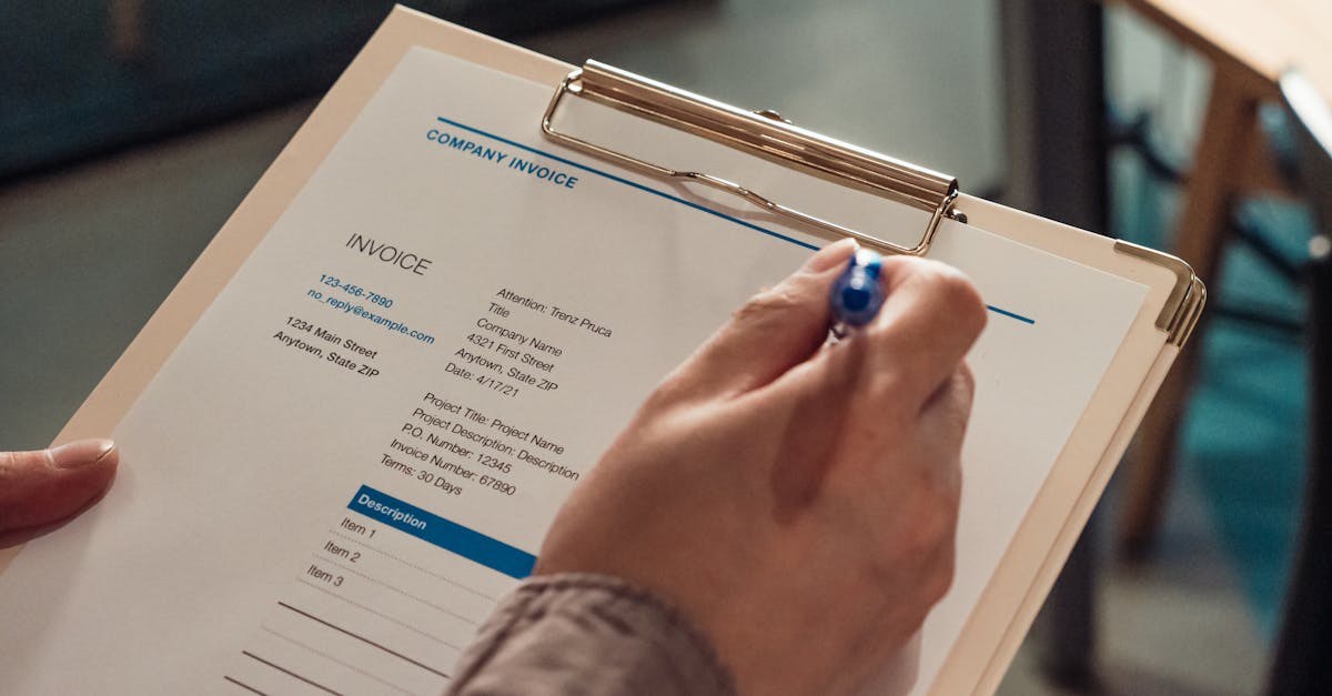Person's hand holding a company invoice on a clipboard with a pen.