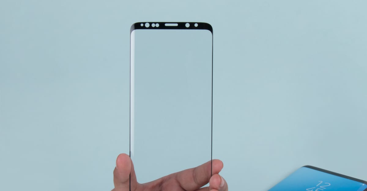Close-up of a hand holding a transparent phone screen protector against a blue background.