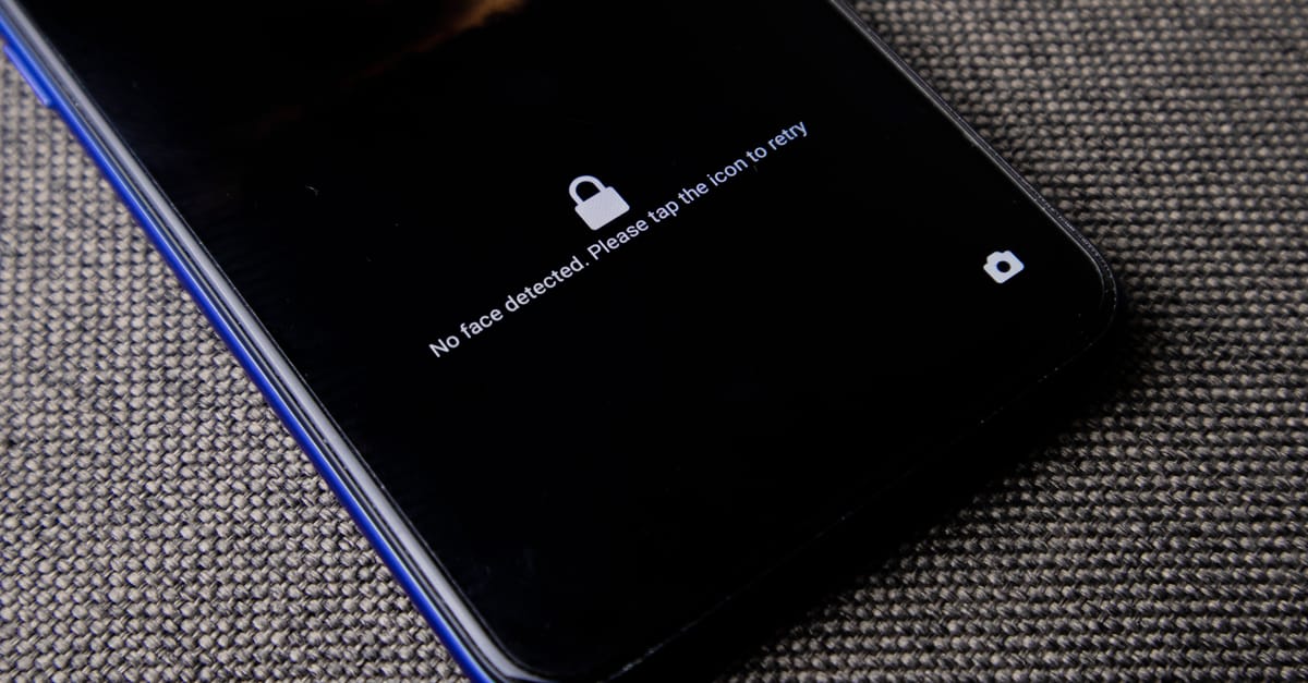 Mobile phone with no face detected message on lock screen on a textured fabric surface.