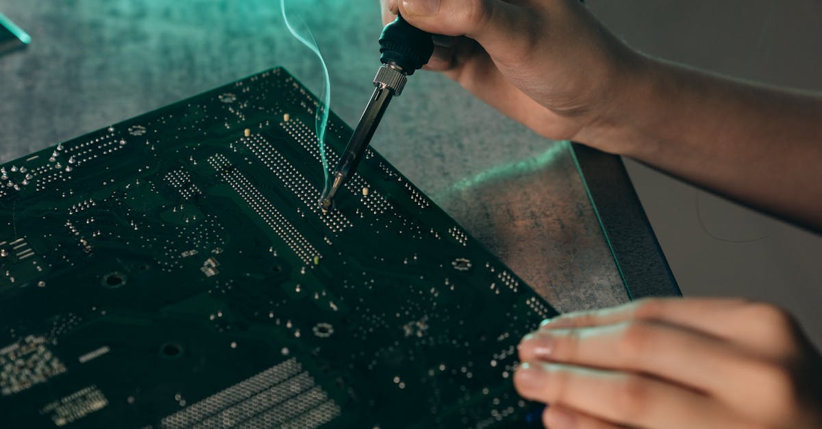 Close-up of hands soldering components on a motherboard with a soldering iron.